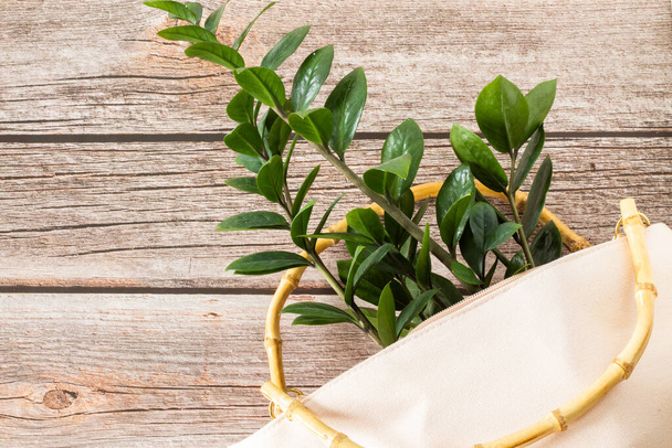 Umweltfreundliche Mehrwegtasche mit Bambusgriffen und frischer Pflanze mit grünen Blättern auf hölzernem Tischhintergrund. Das Konzept von Nachhaltigkeit, Recycling, plastikfreiem Lebensstil, ethischem Konsum - Foto, Bild