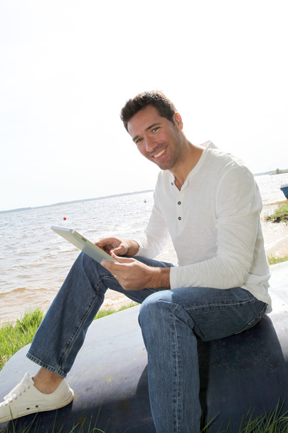 Homem sentado à beira do lago com tablet eletrônico
 - Foto, Imagem