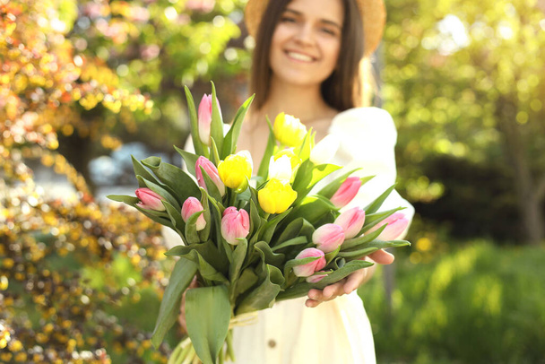 Beautiful young woman with bouquet of tulips in park, focus on flowers - Foto, afbeelding
