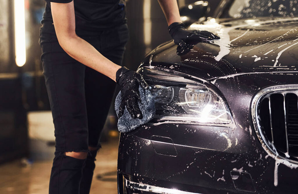 Close up view of vehicle getting wiped. Modern black automobile get cleaned by woman inside of car wash station. - 写真・画像