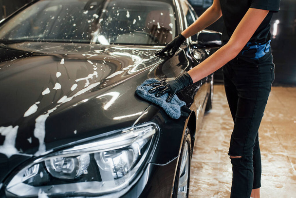 Zbliżenie widoku wycierającego się pojazdu. Nowoczesny czarny samochód się oczyścić przez kobietę wewnątrz stacji myjni samochodowej. - Zdjęcie, obraz