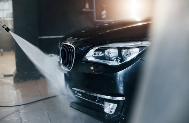 High pressured water. Modern black automobile get cleaned inside of car wash station. - Foto, afbeelding