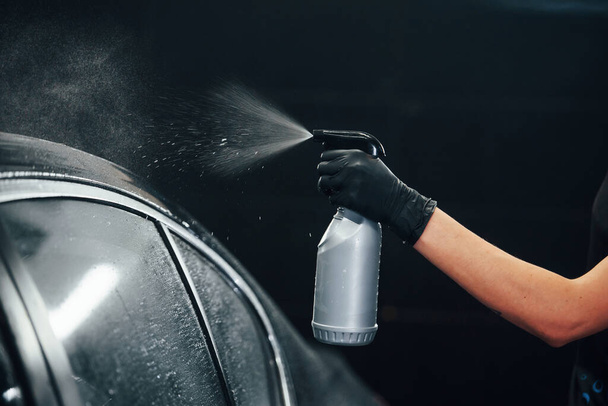 Spraying the vehicle. Modern black automobile get cleaned by woman inside of car wash station. - Φωτογραφία, εικόνα