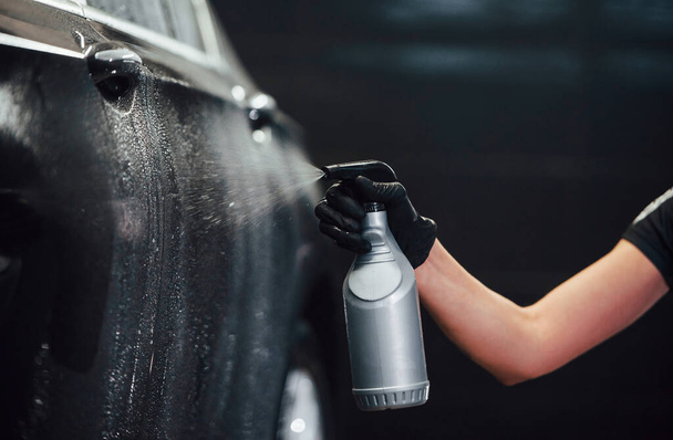 Ψεκάζω το όχημα. Σύγχρονη μαύρο αυτοκίνητο να καθαριστεί από τη γυναίκα στο εσωτερικό του πλυντηρίου αυτοκινήτων σταθμό. - Φωτογραφία, εικόνα