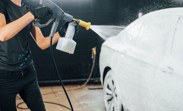 Using high pressure water. Modern black automobile get cleaned by woman inside of car wash station. - Foto, afbeelding