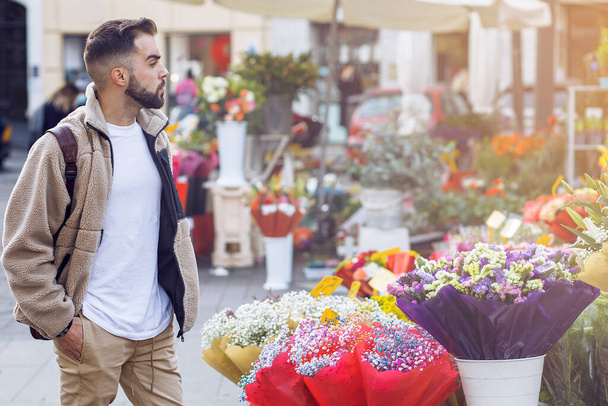 young man strolling down the street and looking at the stalls selling flowers - Photo, image