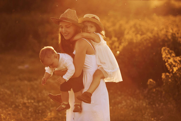 Happy family of mother, little son and daughter spending free time on the field at sunny day time of summer. - Foto, Imagem