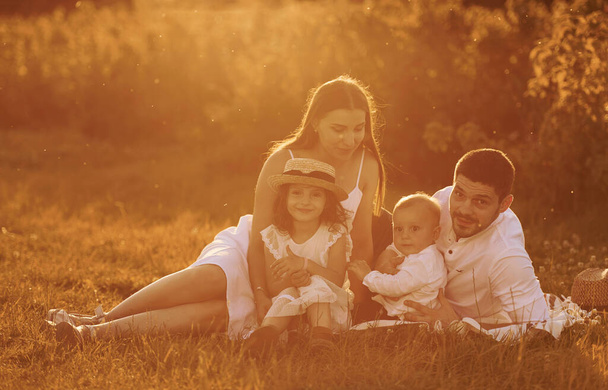 Sitting on the grass. Father, mother with daughter and son spending free time outdoors at sunny day time of summer. - Φωτογραφία, εικόνα