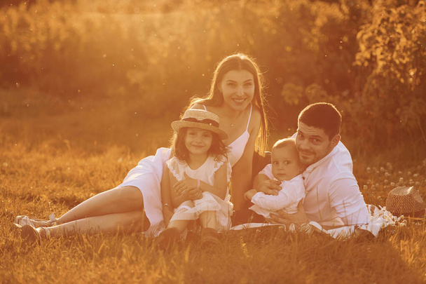 Сидить на траві. Батько, мати з дочкою і сином проводять вільний час на відкритому повітрі в сонячний день під час літа
. - Фото, зображення