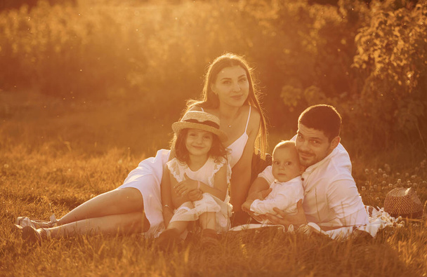 Sitting on the grass. Father, mother with daughter and son spending free time outdoors at sunny day time of summer. - Zdjęcie, obraz
