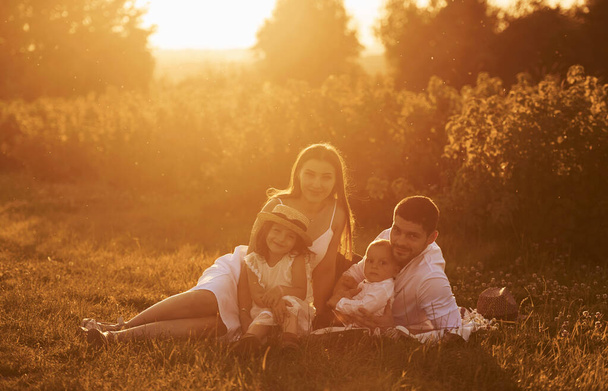 Sitting on the grass. Father, mother with daughter and son spending free time outdoors at sunny day time of summer. - Photo, Image