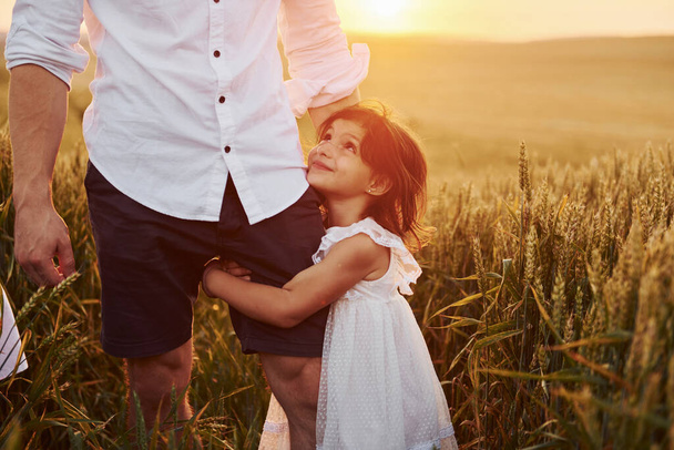 Girl embraces parent. Father with daughter spending free time on the field at sunny day time of summer. - Foto, imagen