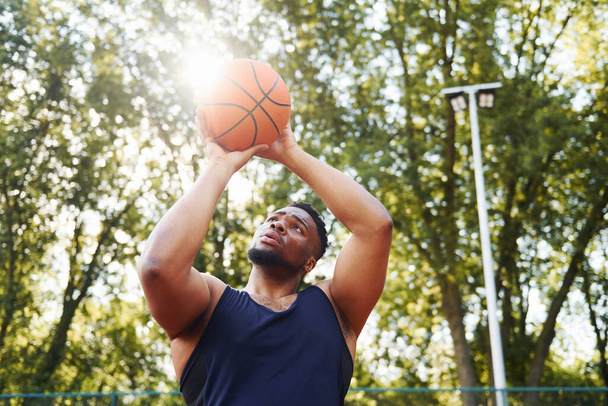 Beautiful green trees on background. African american man plays basketball on the court outdoors. - Foto, Imagem