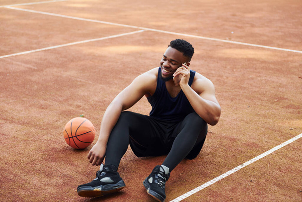 Talks by phone. African american man plays basketball on the court outdoors. - Zdjęcie, obraz