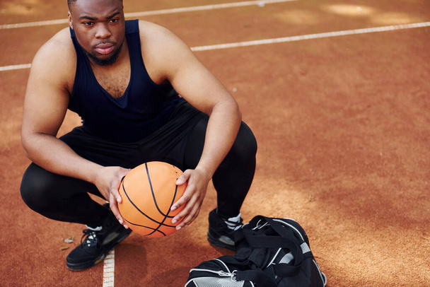 Sits with black bag and preparing for the game. African american man plays basketball on the court outdoors. - Fotografie, Obrázek