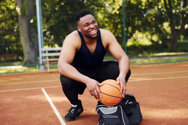 Sits with black bag and preparing for the game. African american man plays basketball on the court outdoors. - Foto, afbeelding