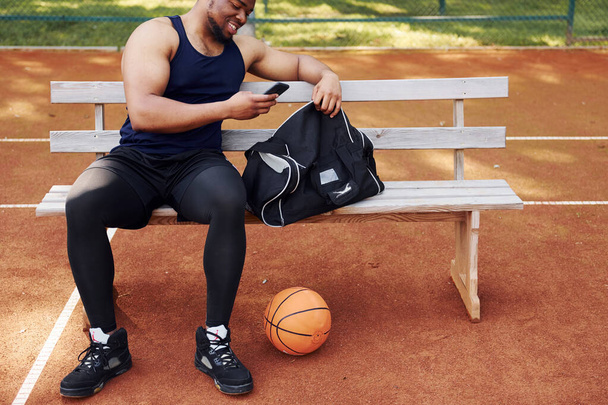 Sits with black bag and preparing for the game. African american man plays basketball on the court outdoors. - Foto, immagini
