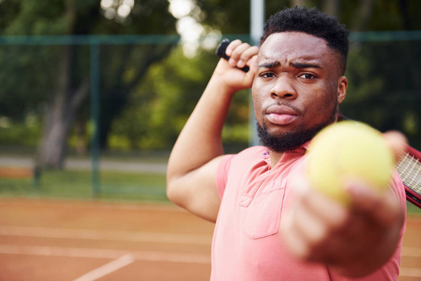 Африканский американец в розовой рубашке играет в теннис на открытом воздухе на корте. - Фото, изображение