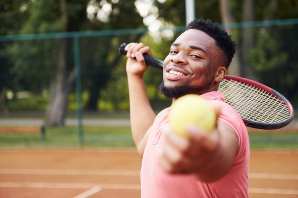 African american man in pink shirt plays tennis on the court outdoors. - Photo, image