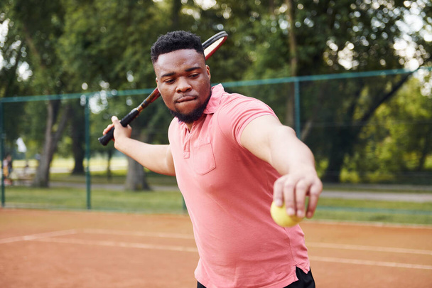 African american man in pink shirt plays tennis on the court outdoors. - Foto, Imagem