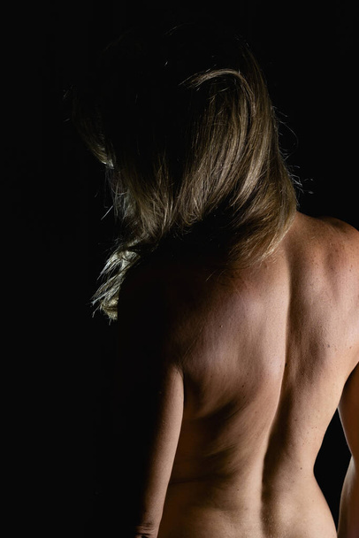 Woman with her back to the camera against black background in studio. Salvador, Bahia, Brazil. - Foto, imagen