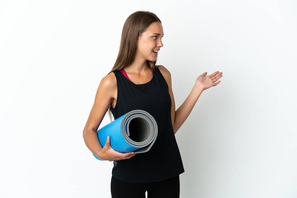 Sport woman going to yoga classes while holding a mat over isolated white background with surprise expression while looking side - Valokuva, kuva