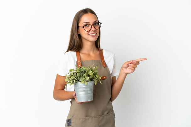Садівник дівчина тримає рослину над ізольованим білим тлом, вказуючи пальцем на бік
 - Фото, зображення
