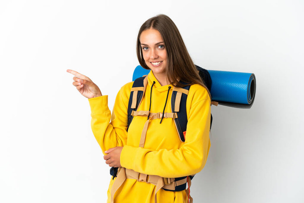 Mladý horolezec žena s velkým batohem přes izolované bílé pozadí ukazující prstem na stranu - Fotografie, Obrázek