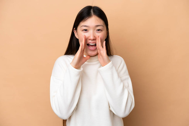 jonge Chinese vrouw geïsoleerd op beige achtergrond schreeuwen en aankondigen iets - Foto, afbeelding