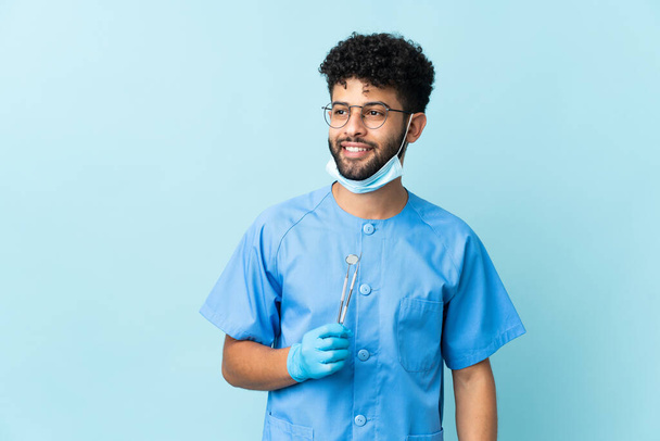 Марокканський стоматолог тримає інструменти ізольовані на синьому фоні, думаючи про ідею під час пошуку - Фото, зображення