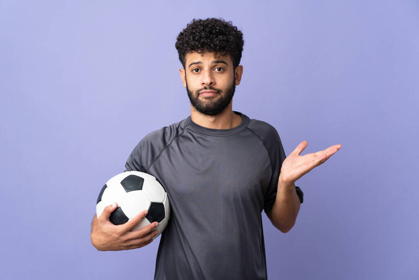 Knappe Marokkaanse jonge voetballer man over geïsoleerd op paarse achtergrond met twijfels terwijl het verhogen van de handen - Foto, afbeelding