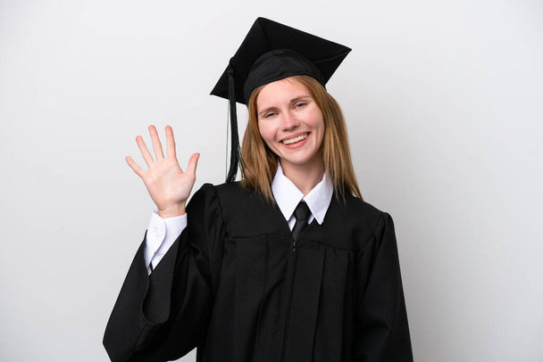 Jeune diplômée universitaire anglaise isolée sur fond blanc saluant à la main avec une expression heureuse - Photo, image