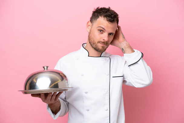 Young Brazilian chef with tray isolated on pink background having doubts - Photo, Image