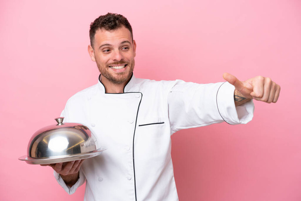 Joven chef brasileño con bandeja aislada sobre fondo rosa dando un gesto de pulgar hacia arriba - Foto, imagen