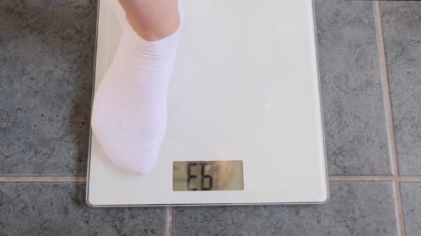 Woman legs in white socks stand on digital scales to check weight on floor in room. - Metraje, vídeo