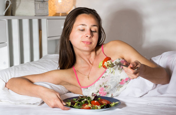 Portrait of lady eating vegetable salad in bed at home - Foto, Imagen