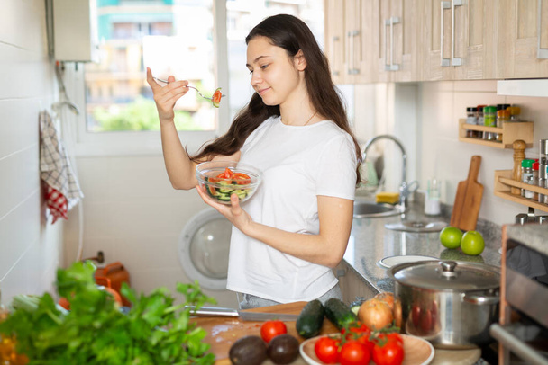 Young woman eating vegetable salad in kitchen - Photo, Image