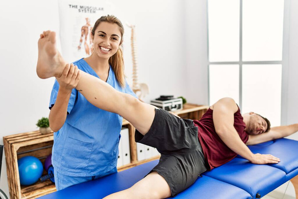 Genç İspanyol fizyoterapist kadın klinikteki adama bacak rehabilitasyonu yapıyor.. - Fotoğraf, Görsel