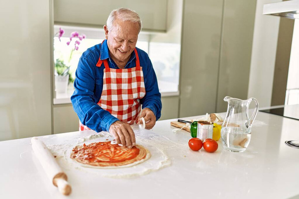 Senior man smiling confident cooking pizza at kitchen - Photo, Image