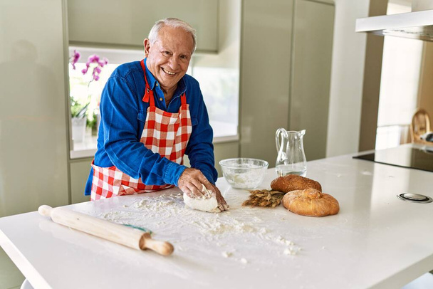 Idősebb férfi mosolyog magabiztos kaparós tészta kezekkel a konyhában - Fotó, kép