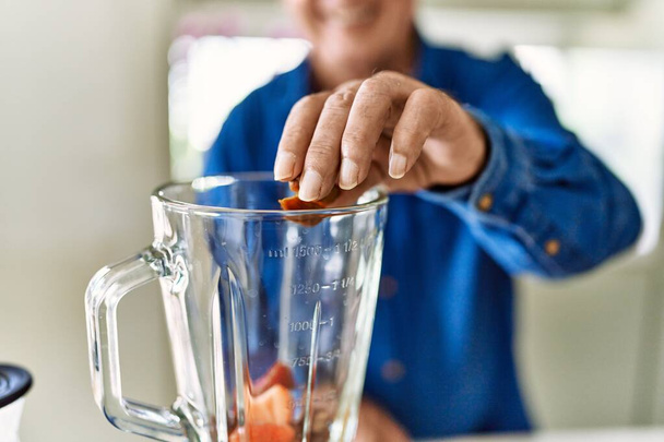 Senior man smiling confident putting datil in blender at kitchen - Foto, imagen