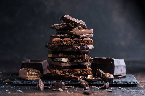 Bar of Chocolate tower pieces. Hazelnut and almond dark chunks of broken chocolate. Sweet food photo concept. - Фото, зображення