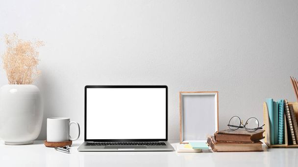 Удобное рабочее место с ноутбуком, рамка, цветочный горшок, чашка кофе и канцелярские принадлежности на белом столе - Фото, изображение