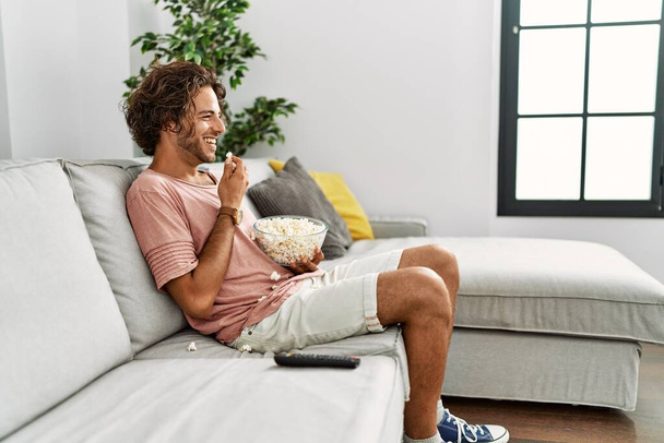Young hispanic man watching movie sitting on the sofa at home. - Zdjęcie, obraz