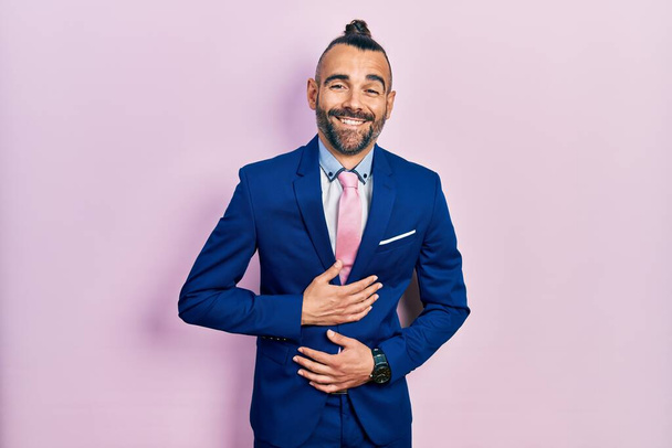 Junger hispanischer Mann in Businessanzug und Krawatte lächelt und lacht laut, weil lustig verrückter Witz mit den Händen am Körper.  - Foto, Bild