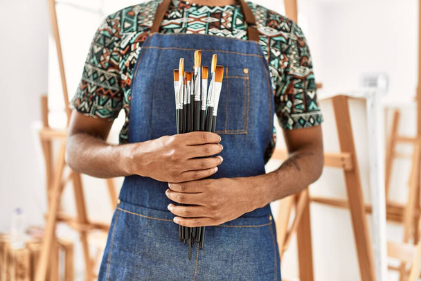 Молодий афроамериканець, який тримає пензлики в художній студії.. - Фото, зображення