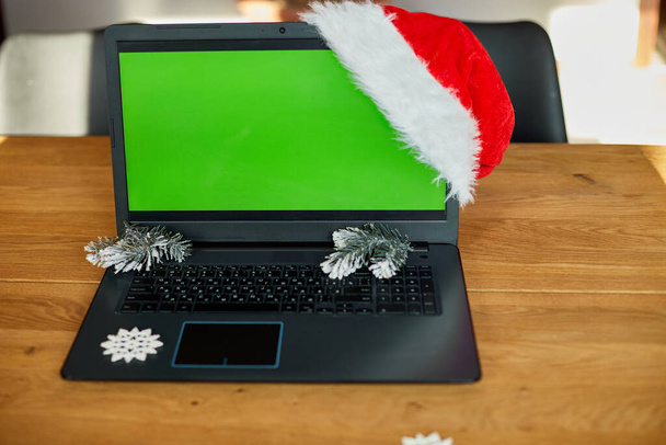 Magasins de Noël concept en ligne, Ordinateur portable avec écran vert placé sur la table avec des cadeaux décorés de Noël, Vue de la table du bureau avec ordinateur portable, coffrets cadeaux - Photo, image