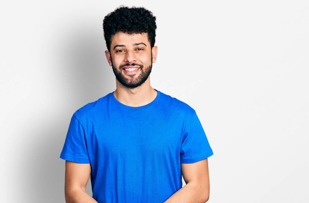 Nuori arabimies, jolla on parta yllään rento sininen t-paita kädet yhdessä ja ristissä sormet hymyillen rento ja iloinen. menestys ja optimistinen  - Valokuva, kuva