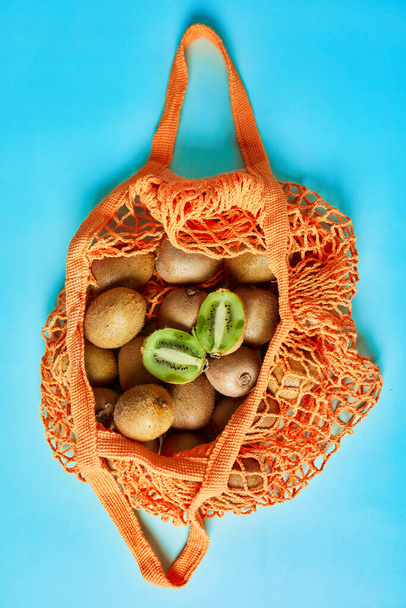 Flat lay Mesh grocery  shopping eco friendly bag with kiwi on blue canvas background, Zero waste cconcept, Local farmers market, shopping mall, top view, copy space, Plastic free items. - Foto, imagen