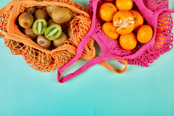 Flat lay Mesh grocery  shopping eco friendly bag with kiwi and tangerine fruits on green canvas background, Zero waste cconcept, Local farmers market, shopping mall, top view, copy space, Plastic free items. - 写真・画像